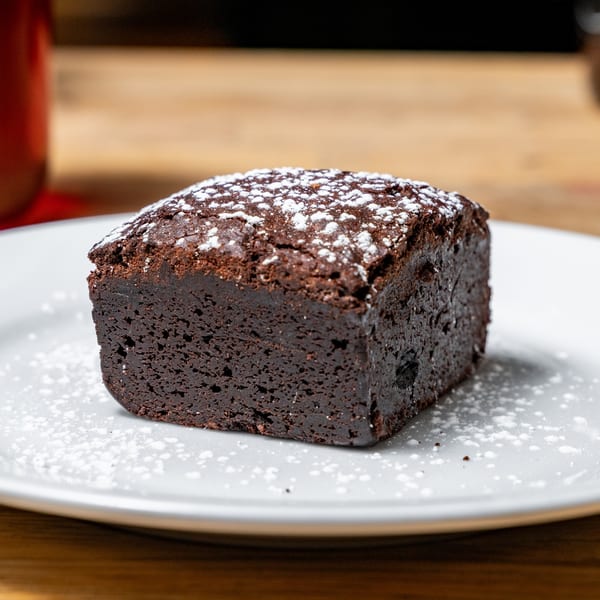 A rich, dark chocolate brownie dusted with powdered sugar on a white plate.