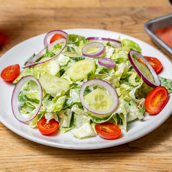 Side salad with lettuce, sliced cucumbers, red onions, and cherry tomatoes on a white plate.