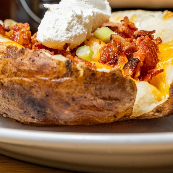 Baked potato with melted cheese, crispy bacon bits, sour cream, and sliced green onions.
