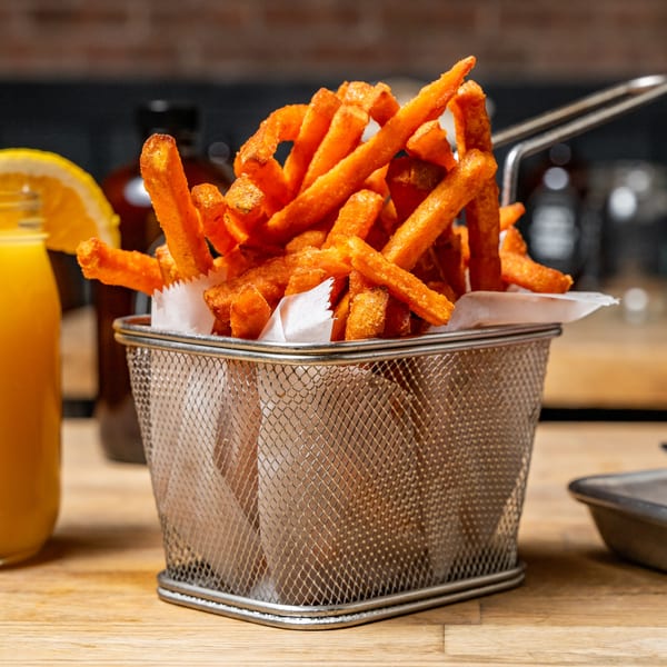 Crispy sweet potato fries in a metal basket with white paper, next to a drink.
